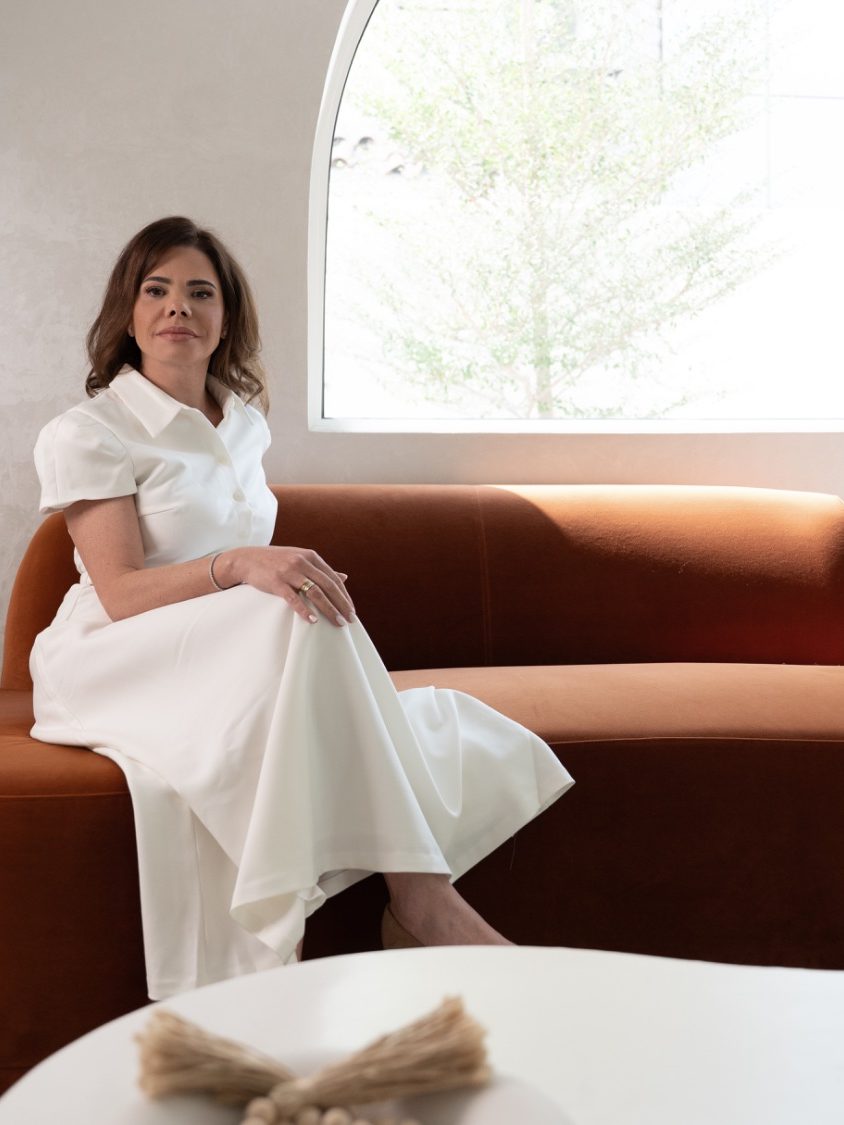 Dr. Lionella Moraes seated on a terracotta velvet sofa in a private clinic lounge