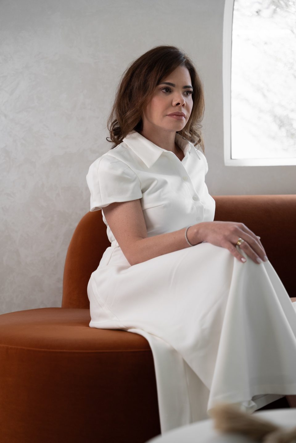 Dr. Lionella Moraes seated in profile on a terracotta sofa by an arched window